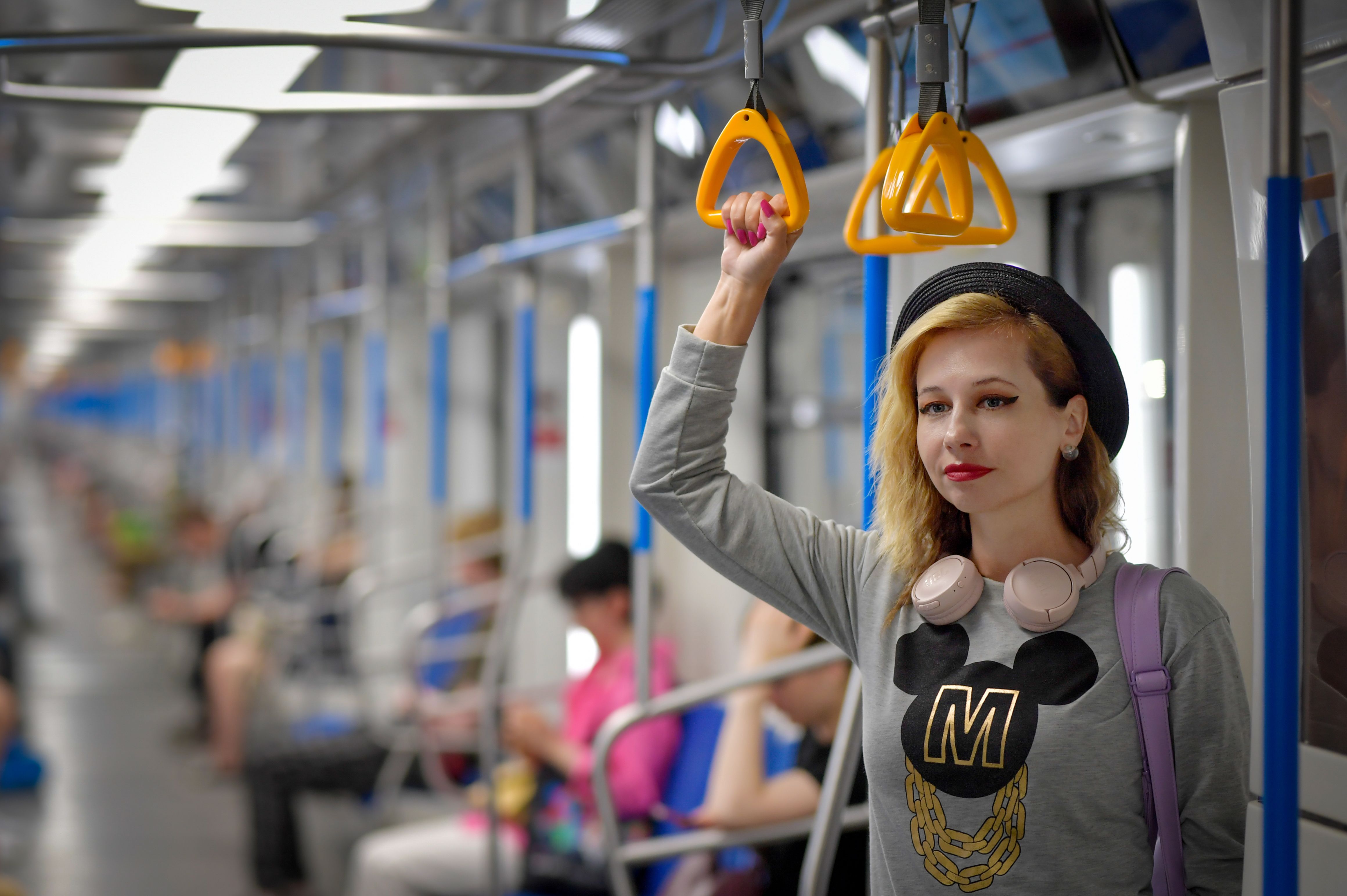 Stylish woman with headphones rides the subway, holding onto handhold in a busy train.