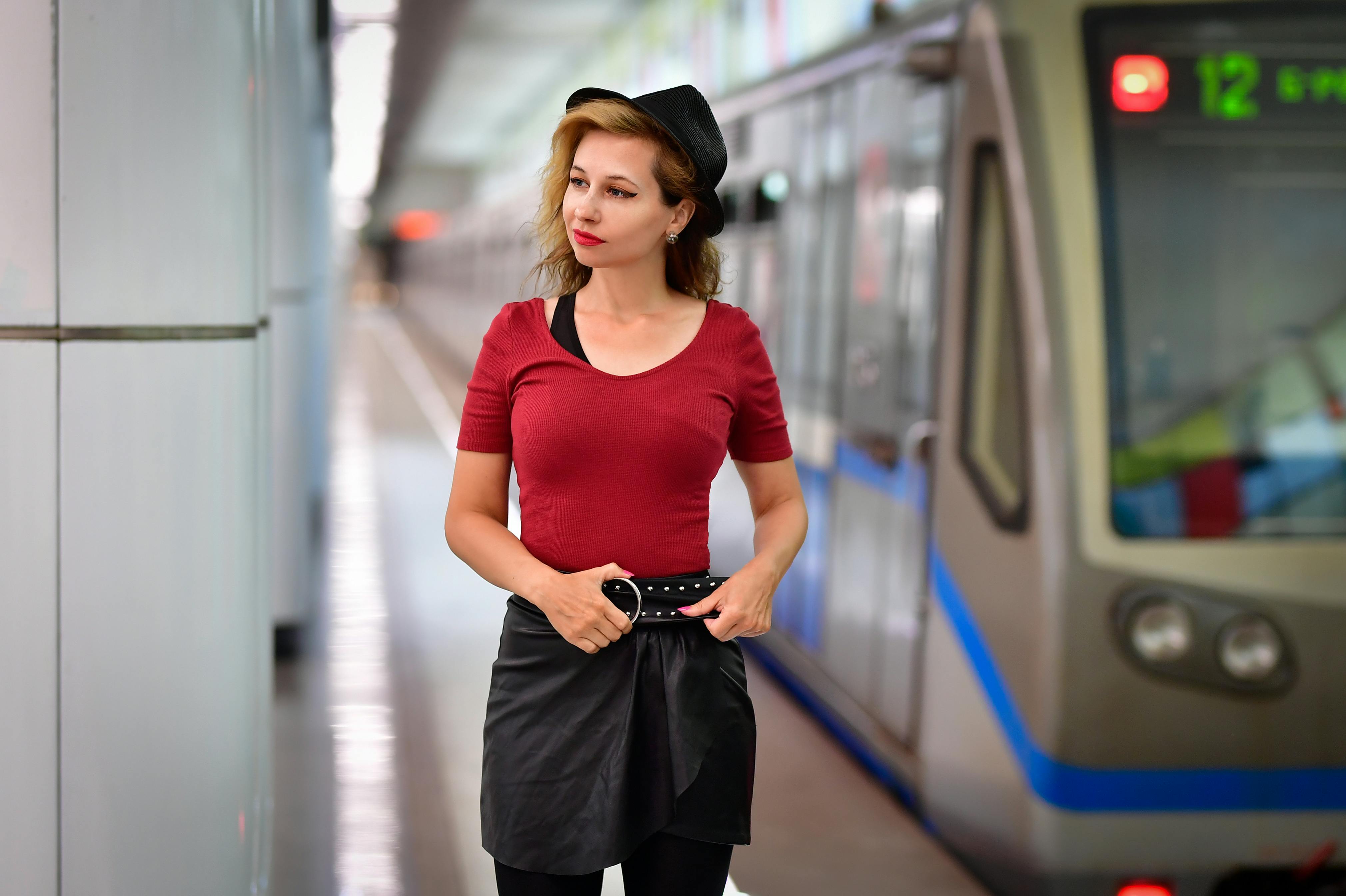 Free Fashionable woman in red top and hat standing by a train in a metro station, exuding modern urban style. Stock Photo