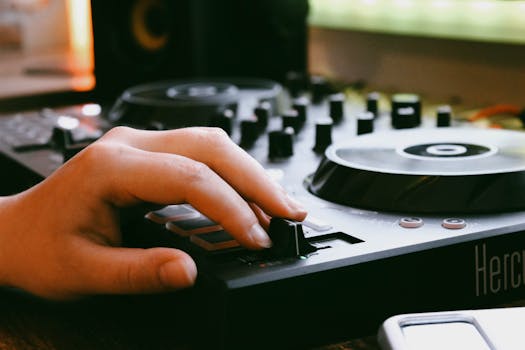 Close-up of a DJ hand adjusting audio mixer controls in a recording studio setting, showcasing modern music equipment.