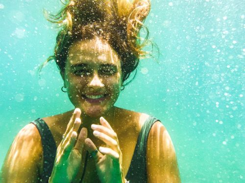 Free A joyful woman swimming underwater, surrounded by bubbles and sunlight, showcasing a carefree vacation moment. Stock Photo