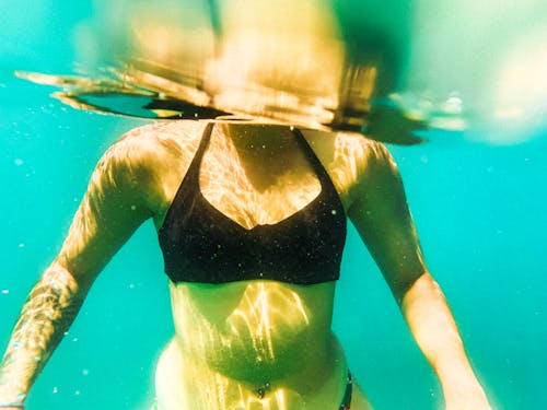 Underwater View of Woman in a Black Bikini Swimming in Blue Water 