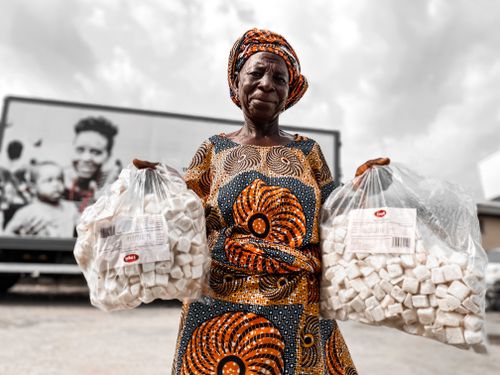 Free African woman in traditional attire displaying bags of local delicacy at an outdoor market. Stock Photo