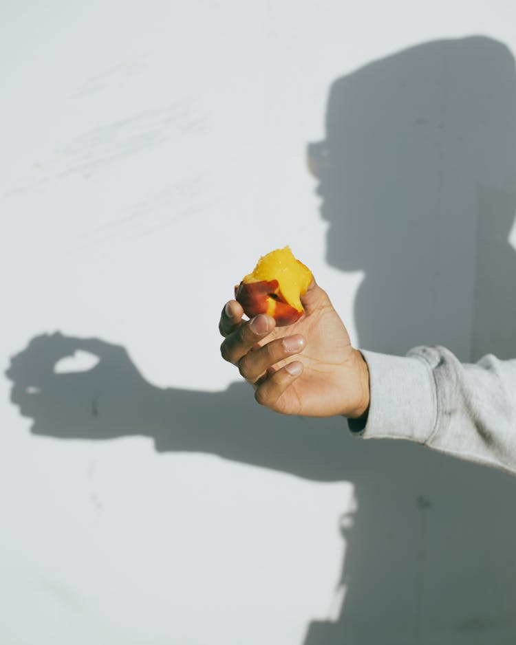 Hand Holding Peach With Shadow On Wall