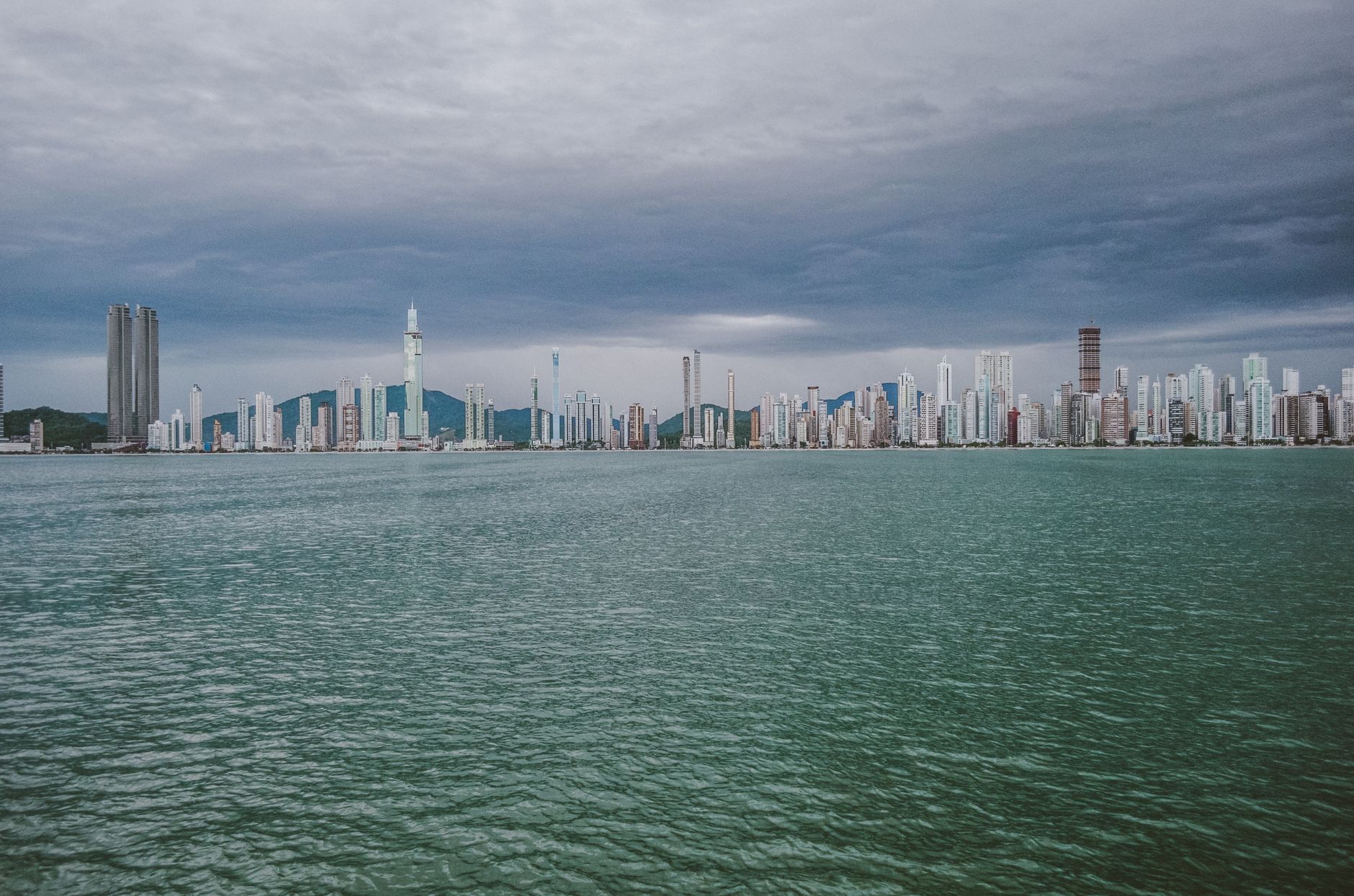 Stunning skyline of Balneário Camboriú, Brazil, viewed from the ocean with skyscrapers under a moody sky.