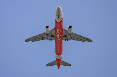 Free Low-angle shot of an AirAsia airplane flying against a bright blue sky. Stock Photo