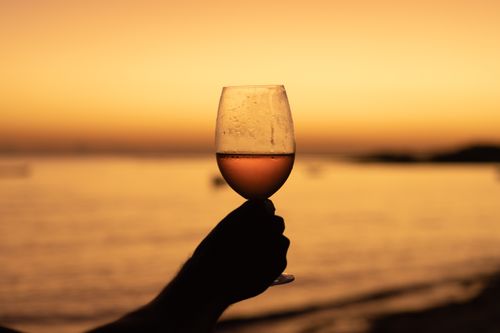 Free A silhouetted hand holding a wine glass against a stunning beach sunset, evoking relaxation. Stock Photo