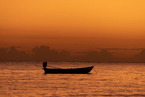 Free Peaceful scene of a boat silhouette against an orange sunset sky over calm sea. Stock Photo