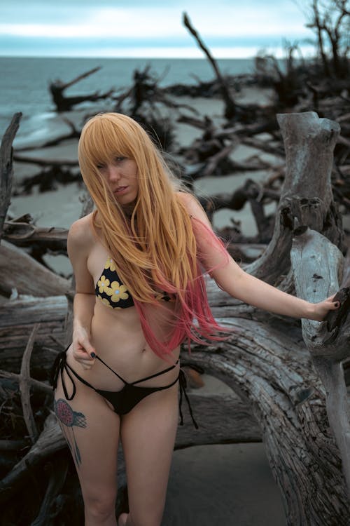 A Woman in Black and Yellow Floral Bikini Leaning on a Driftwood