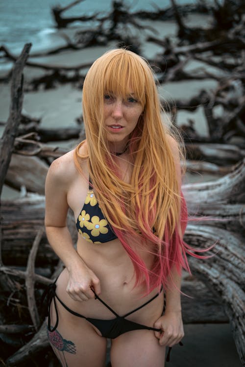 A Woman in Black and Yellow Floral Bikini Standing Beside a Driftwood
