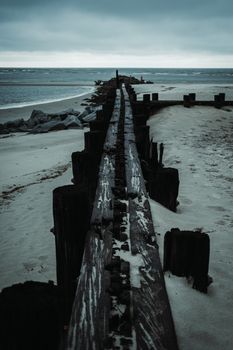 Dark, atmospheric beach boardwalk leading to the ocean under a cloudy sky.