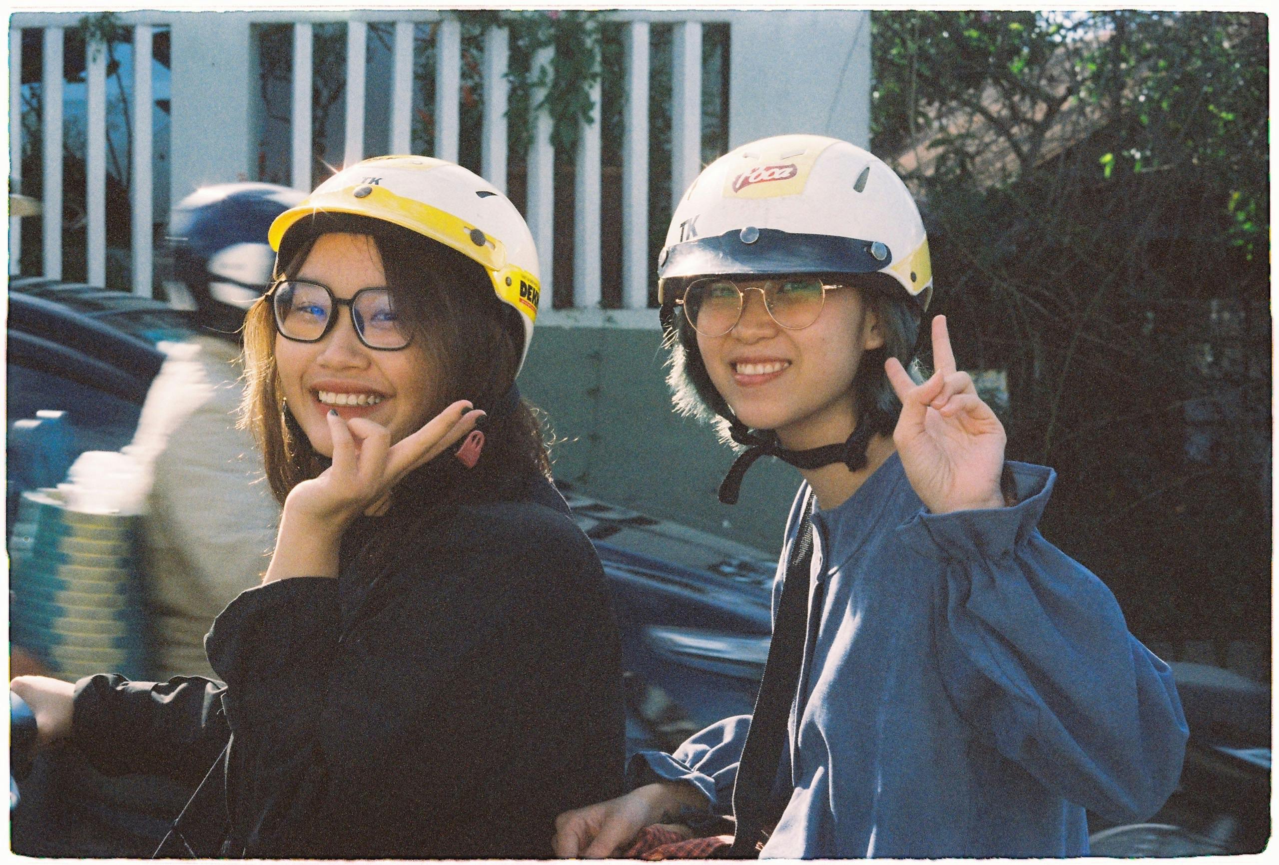 Two women wearing helmets and glasses, smiling and posing with peace signs outdoors.