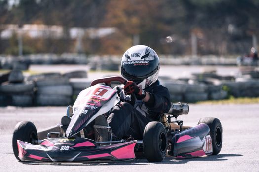 Driver in full gear racing a go-kart on a sunny outdoor track, showcasing speed and skill.