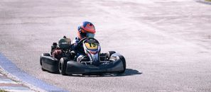 A young racer in a go-kart speeding on a sunlit track, showcasing competitive racing action.