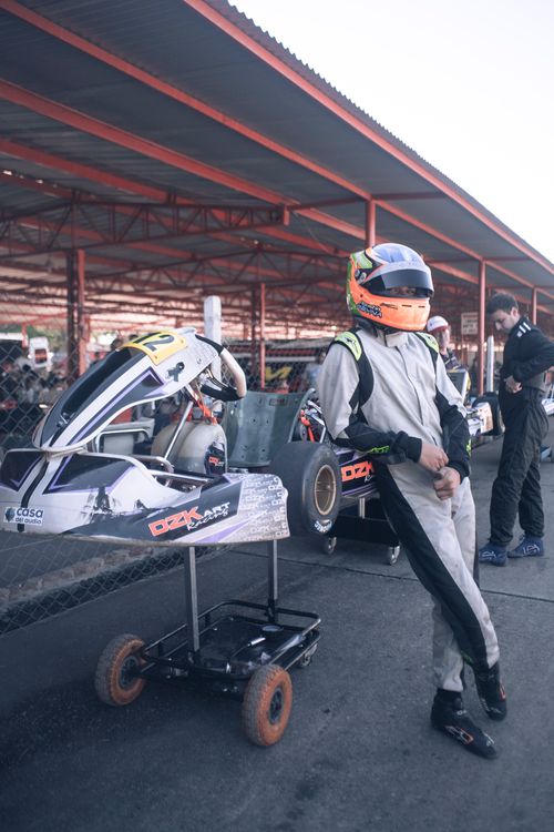 Free A young racer in full gear stands by a go-kart in the pit area, ready for competition. Stock Photo