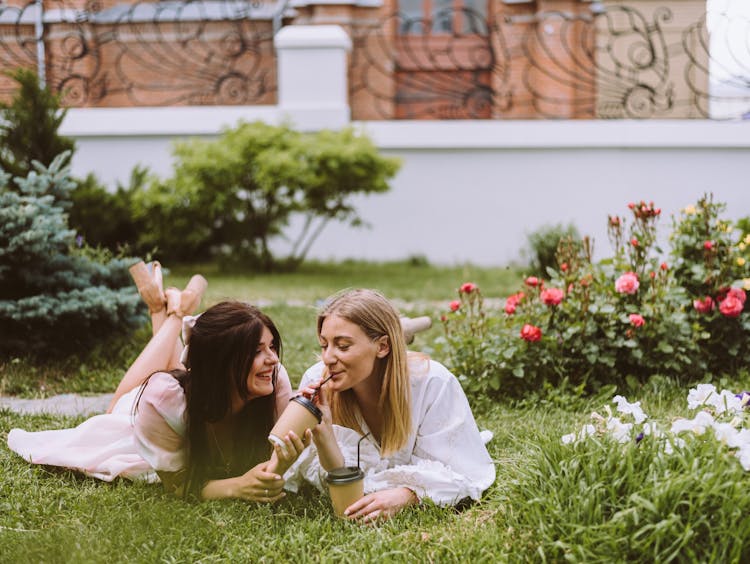 Happy Girls Lying On Grass Drinking Takeaway Coffee