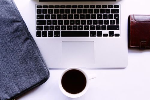 Free A neat workspace with a silver laptop, cup of black coffee, and leather wallet on a white desk. Stock Photo