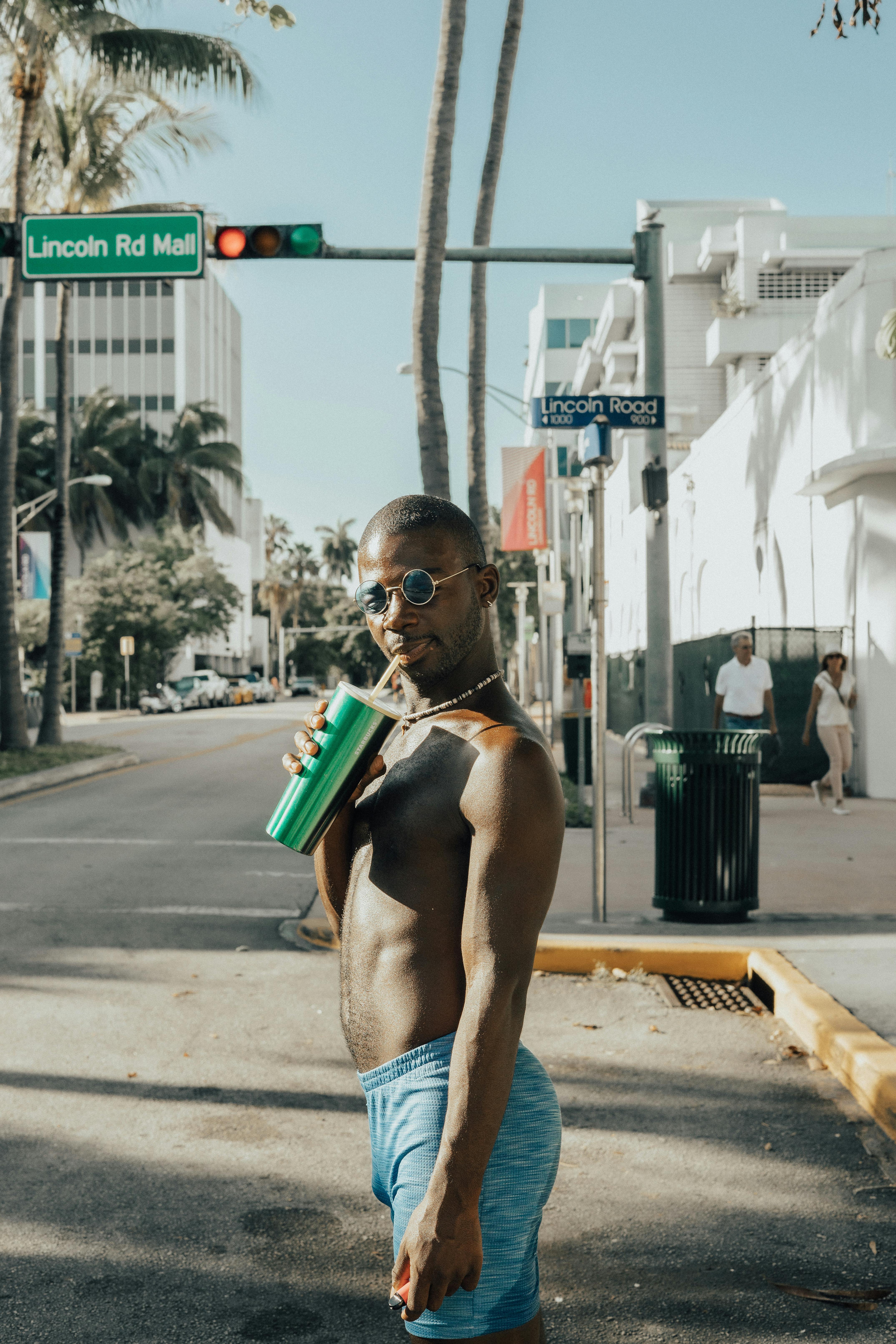 naked man drinking beverage on city street