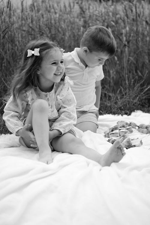 Grayscale Photo of Two Children Sitting on White Picnic Blanket