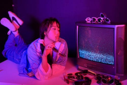 Free Young woman in vibrant lighting with retro TV and stylish sunglasses, embodying a casual and modern vibe. Stock Photo