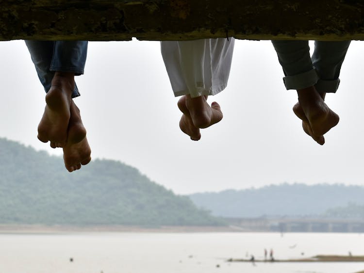 Legs Hanging Against River Among Hills