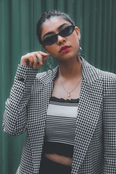 Stylish woman in sunglasses and plaid jacket posing confidently outdoors.