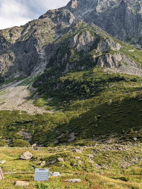 Scenic view of towering rocky mountains with a lush green valley below under a sunny sky.
