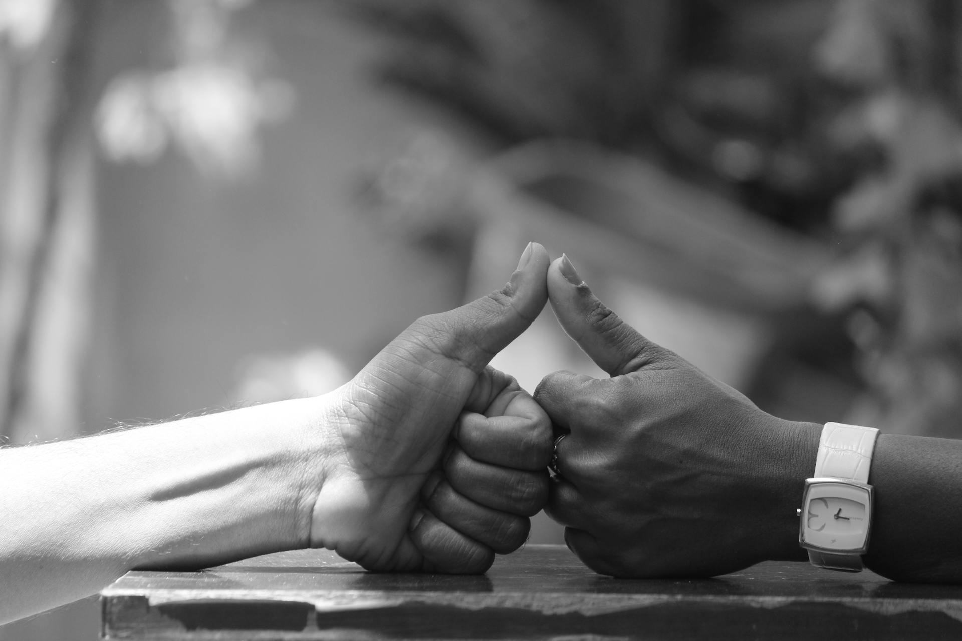 Black and white close-up of two hands interlocking thumbs in a friendly gesture.