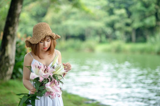 宁静的湖边，一位戴着草帽的年轻女子拿着一束百合花