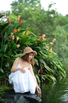 A serene portrait of a young woman in a white dress sitting by a stream, surrounded by lush greenery.