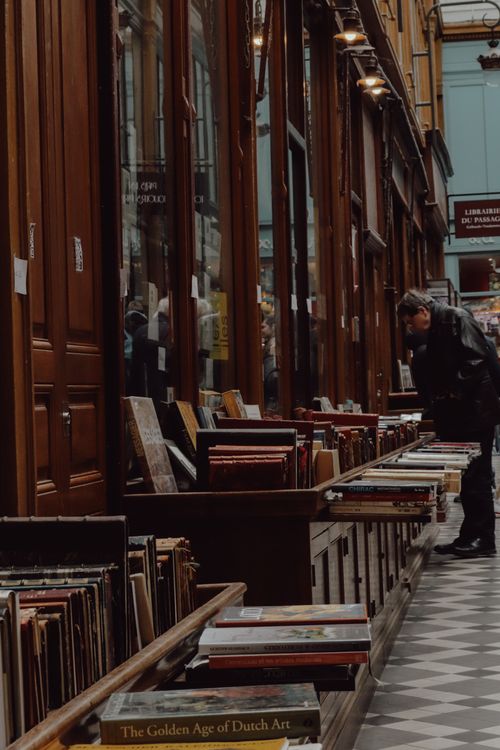 Free Man browsing books in a Parisian bookstore alley, rich with reflections and vintage charm. Stock Photo