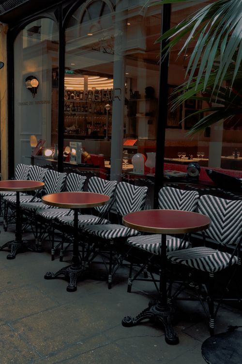 Free Exterior view of a Paris café with outdoor seating, featuring round tables and chevron-patterned chairs. Stock Photo