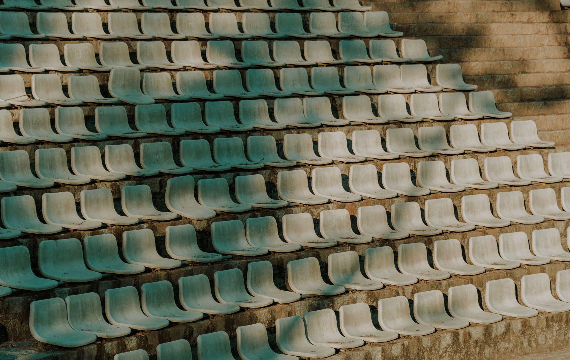 Rows of empty plastic seats arranged in an outdoor stadium setting.