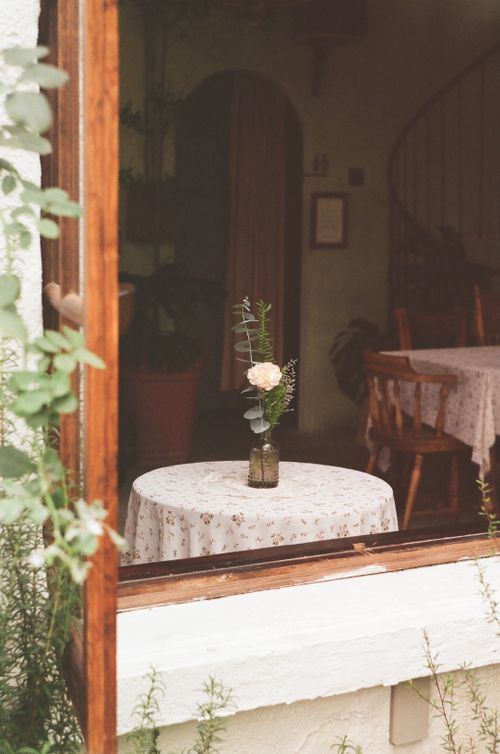 Free Charming rustic interior with a table, flower vase, and wooden chairs viewed through a window. Stock Photo