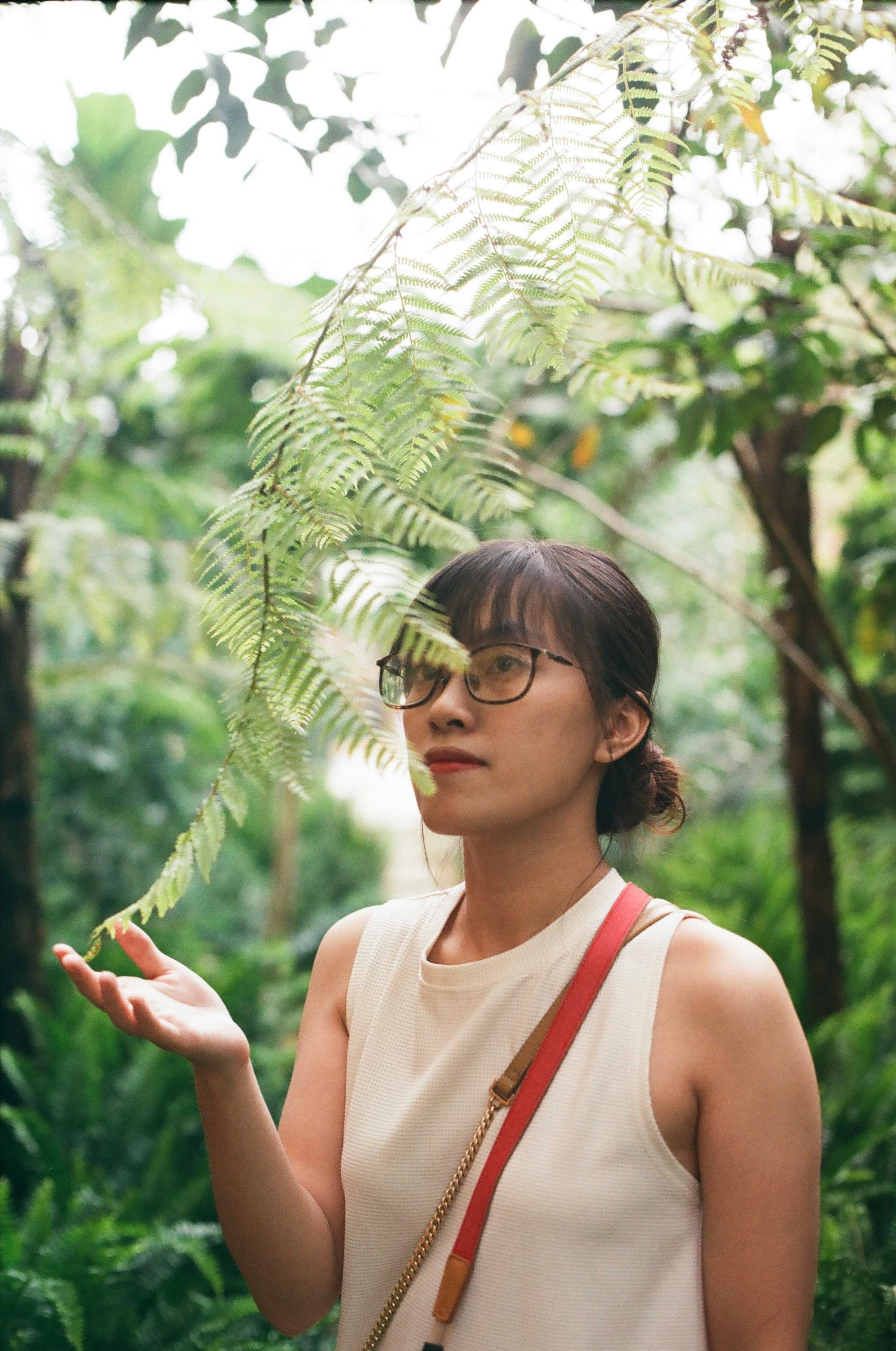 Asian woman in sleeveless top admiring lush green foliage outdoors.