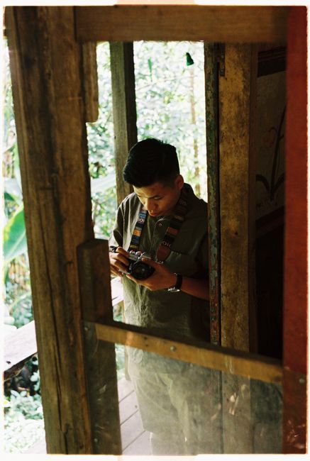 Asian man holding camera in a rustic doorway, looking down intently.