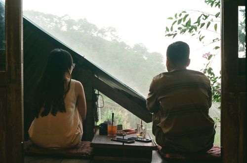 Free A couple sits at a window table enjoying a foggy mountain view, creating a serene moment. Stock Photo