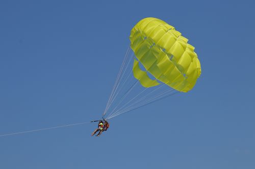 Free Experience the thrill of parasailing with a vibrant yellow parachute against a clear blue sky. Stock Photo