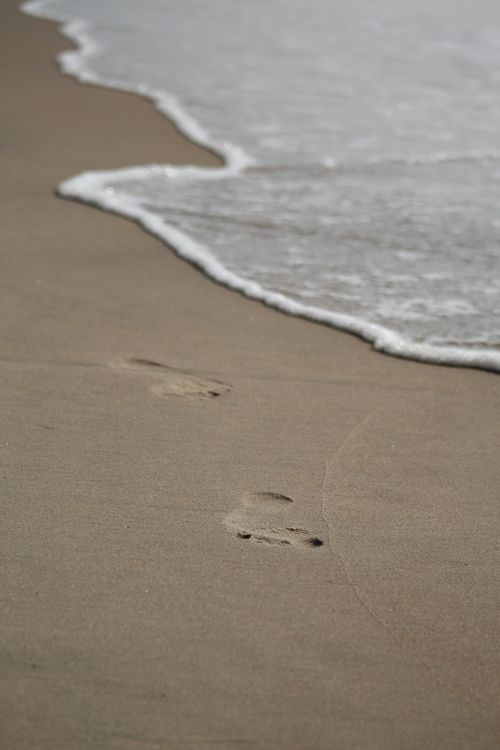 Free Footprints leading into gentle waves at seashore, evoking peace and solitude. Stock Photo