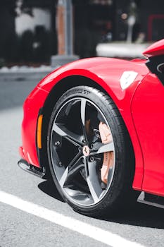 Detailed view of a red sports car wheel with custom rims and brake caliper on urban street.