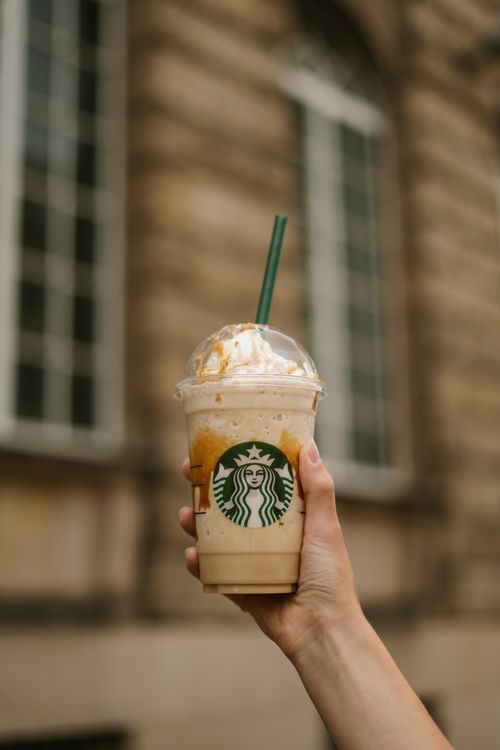 Free Hand holding an iced coffee with whipped cream on a city street background. Stock Photo