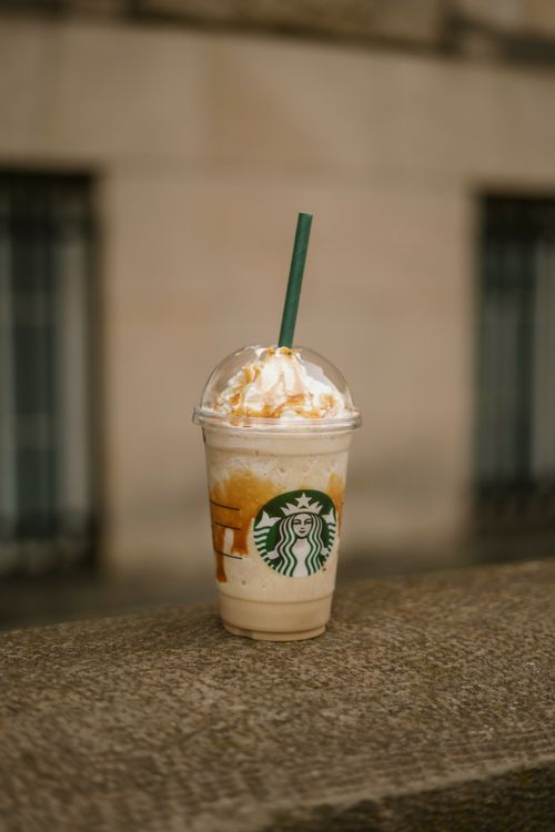 Free Refreshing Starbucks frappe in a plastic cup with whipped cream and caramel drizzle outdoors. Stock Photo