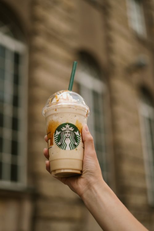 Free Close-up of a hand holding a Starbucks frappuccino with a blurred building backdrop. Stock Photo