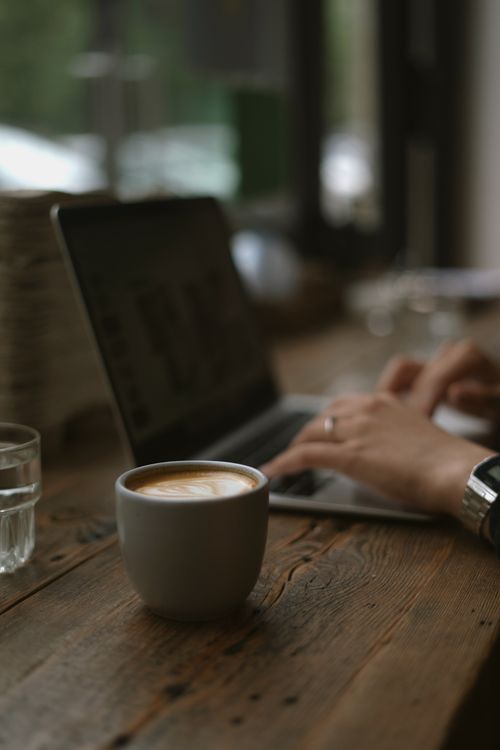 Free A warm, inviting workspace featuring a laptop and a steaming cup of coffee on a wooden table. Stock Photo
