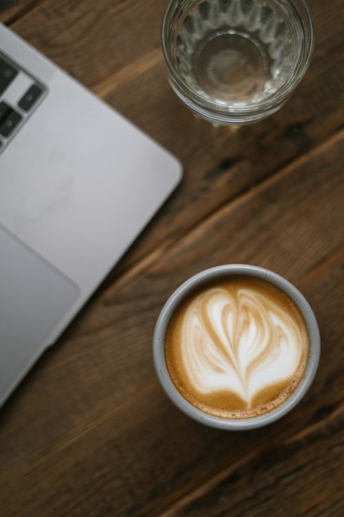 Free A beautifully crafted latte art next to a laptop on a wooden desk. Stock Photo