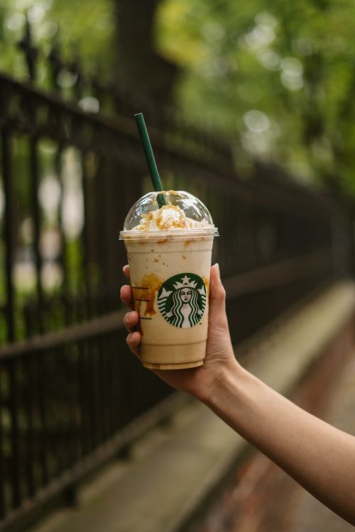 Free Hand holding a Starbucks iced coffee outdoors with a blurred background. Stock Photo