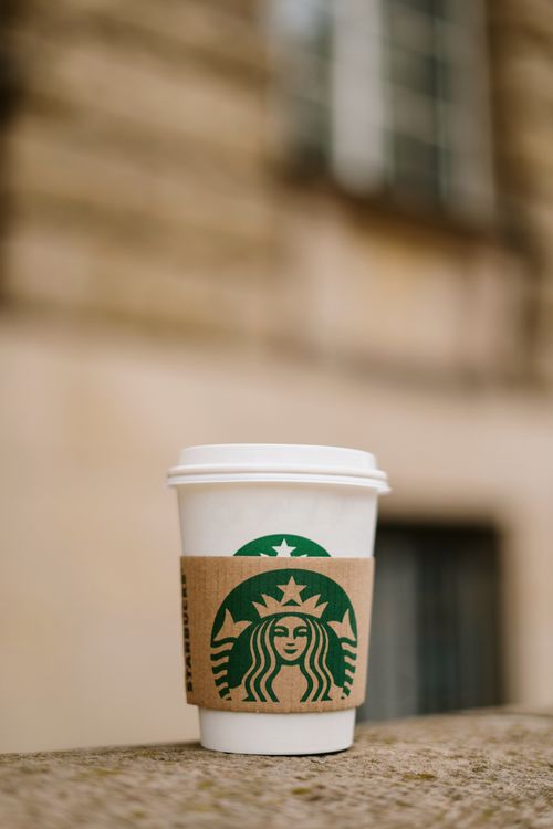 Free A close-up shot of a coffee cup with a branded sleeve against a blurred outdoor background. Stock Photo