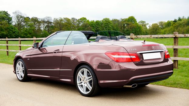 A sleek brown Mercedes-Benz E220 convertible parked on a scenic country road in the UK.