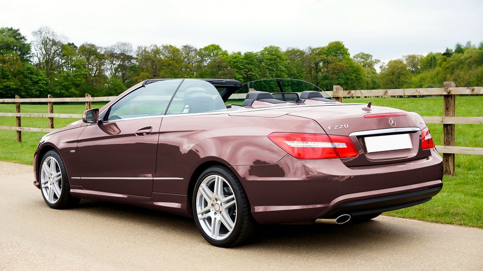 A sleek brown Mercedes-Benz E220 convertible parked on a scenic country road in the UK.