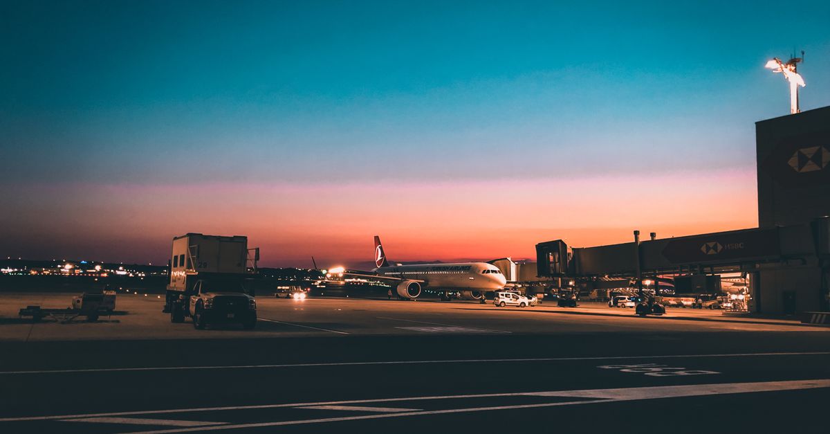 Airplane on airport tarmac during sunset with vibrant, dramatic sky creating a scenic travel mood.