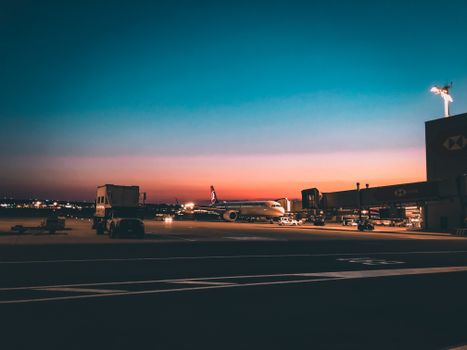 Airplane on airport tarmac during sunset with vibrant, dramatic sky creating a scenic travel mood.